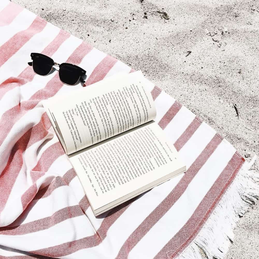 on the beach with an open book and sunglasses in summer 2019white and pink stripe towel